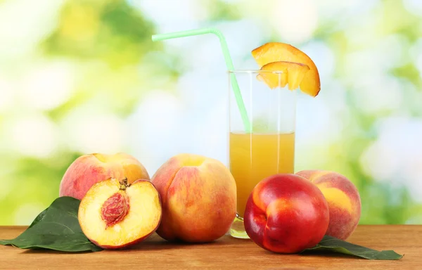 Спелые персики и сок на деревянном столе на естественном фоне — стоковое фото