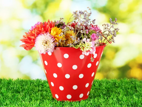 Rode emmer met witte polka-stip met bloemen op groene achtergrond — Stockfoto