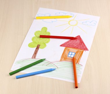 Children's drawing of house and pencils on wooden background clipart