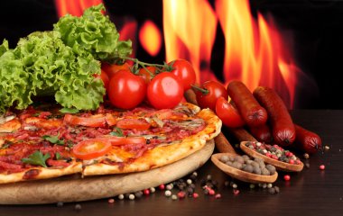 güzel pizza, salam, domates ve baharatlar alev arka plan üzerinde ahşap tablo