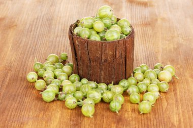 Green gooseberry in wooden cup on wooden background clipart