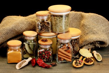 Jars and spoons with spices on wooden table on black background clipart