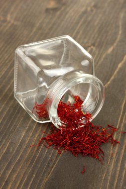 Stigmas of the saffron poured out a glass jar on wooden background close-up clipart