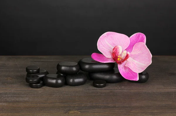Spa stones with orchid flower on wooden table on grey background — Stock Photo, Image