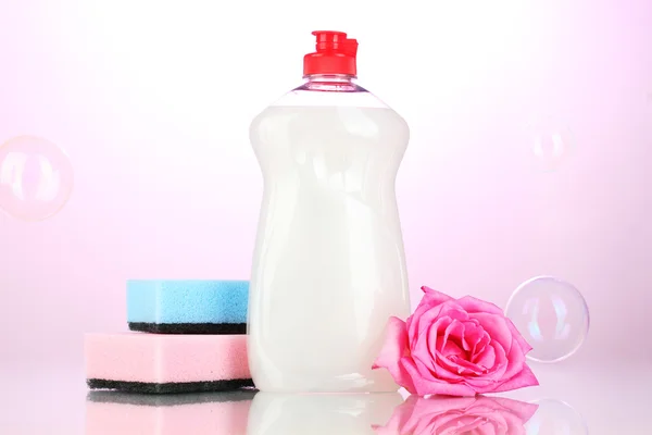 Líquido lavavajillas con esponjas y flores sobre fondo rosa —  Fotos de Stock