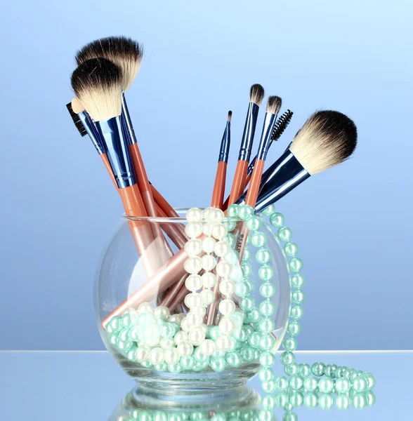 Cepillos de maquillaje en un tazón con collar de perlas sobre fondo azul — Foto de Stock