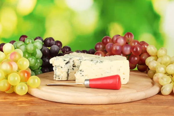 Cheese with mold on the cutting board with grapes on bright green background — Stock Photo, Image