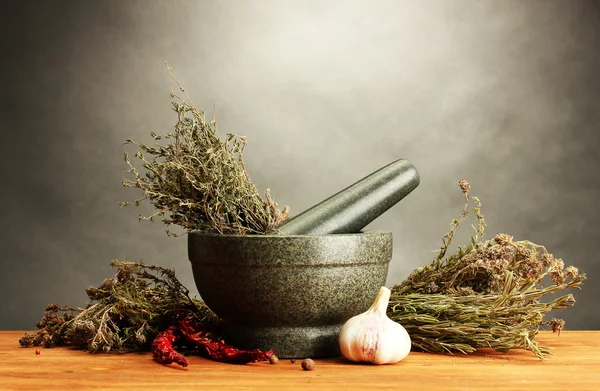 Dried herbs in mortar and vegetables, on wooden table on grey background