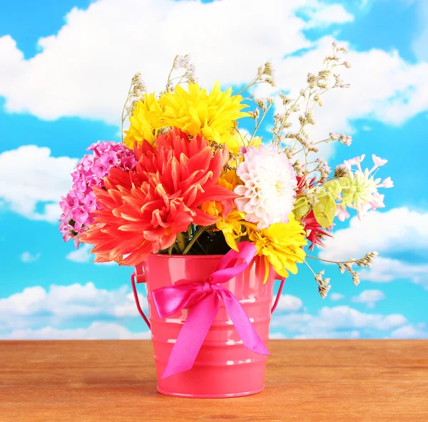 Bright pink bucket with flowers on sky background — Stock Photo, Image