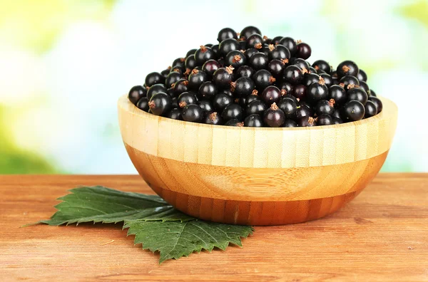 Fresh black currant in wooden bowl on green background close-up — Stock Photo, Image