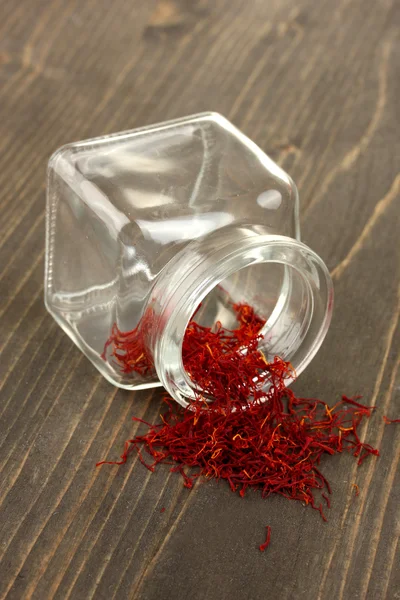 stock image Stigmas of the saffron poured out a glass jar on wooden background close-up