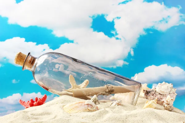 玻璃奶瓶与内部在沙子上，蓝蓝的天空背景上的笔记 — 图库照片