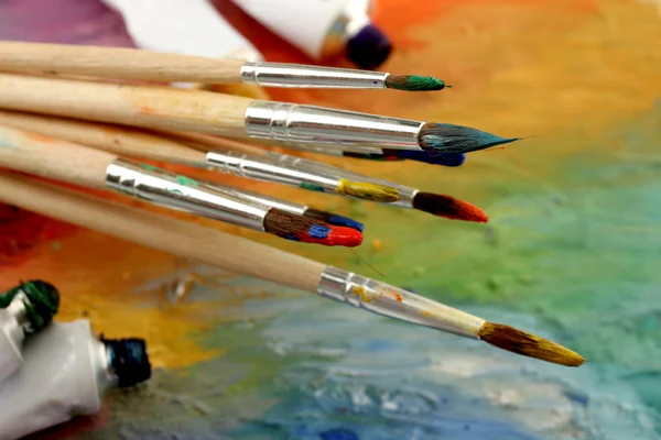 Acrylic paint, paint tubes and brushes on wooden palette — Stock Photo, Image