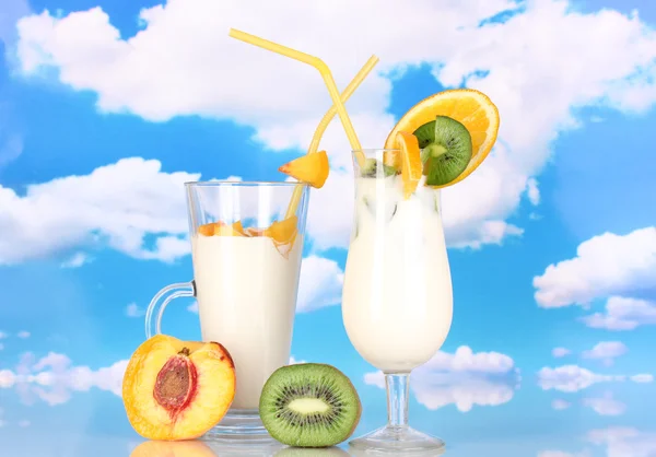 Köstlicher Milchshake mit Früchten auf dem Tisch vor himmelblauem Hintergrund — Stockfoto