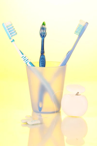 Tandenborstel in glas, tandzijde en kauwgom op gele achtergrond — Stockfoto