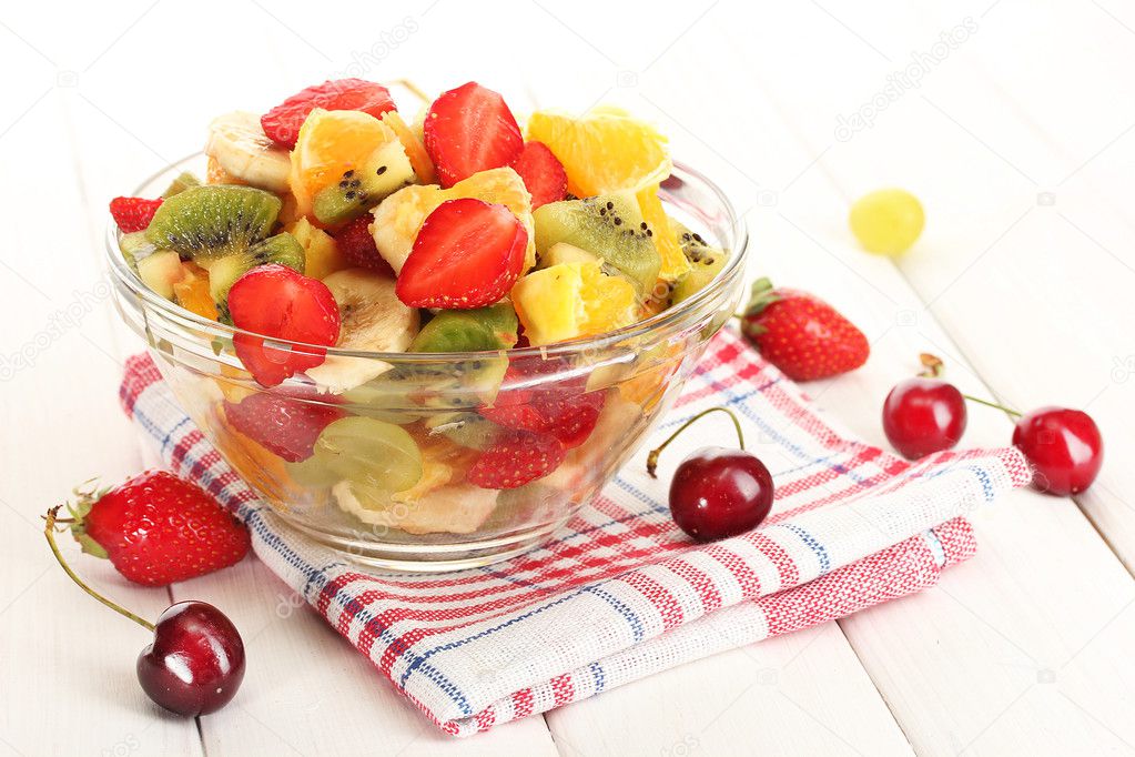 Glass bowl with fresh fruits salad and berries on white wooden table
