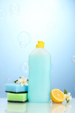 Dishwashing liquid with sponges and lemon with flowers on blue background clipart