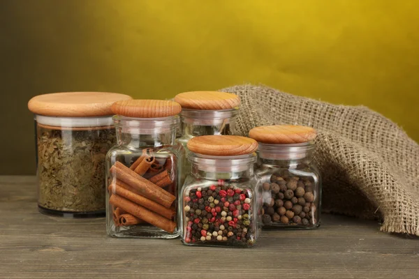 Jars with spices on wooden table on yellow background — Stock Photo, Image