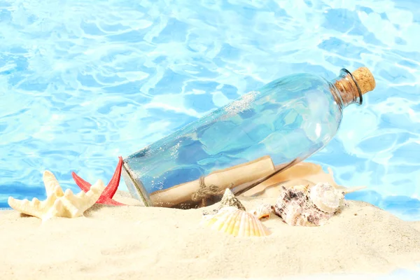 Glazen flesje met opmerking binnen op zand, op blauwe zee achtergrond — Stockfoto