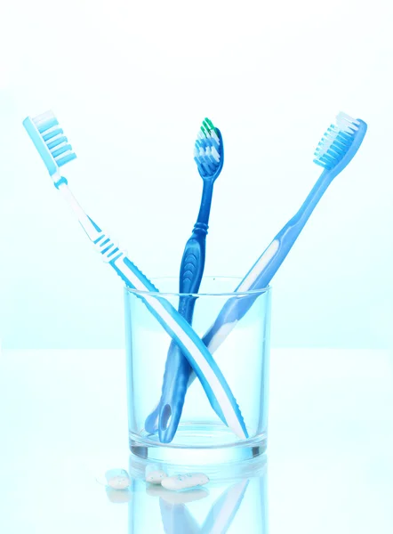 Cepillo de dientes en vidrio y goma de mascar sobre fondo azul —  Fotos de Stock