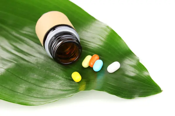 Tabletki na zielony liść z butelki na białym tle — Zdjęcie stockowe