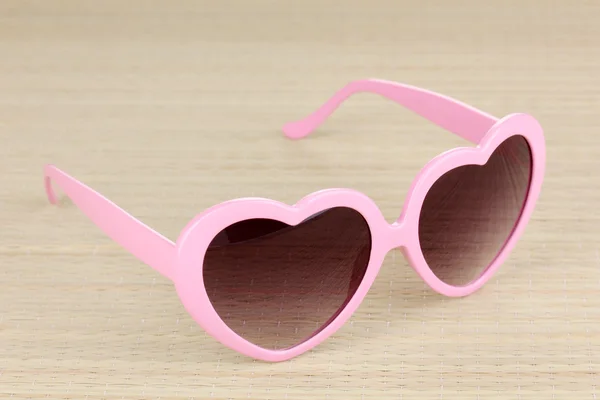Óculos de sol cor-de-rosa em forma de coração no tapete de bambu — Fotografia de Stock