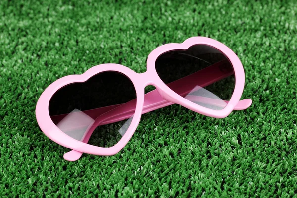 Roze hart-vormige zonnebril op groen gras — Stockfoto