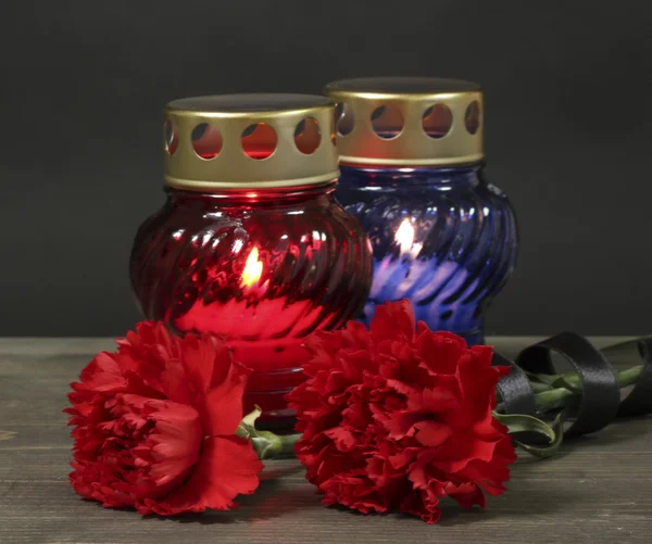 内存灯笼和蜡烛，红色的康乃馨和木制的桌子上灰色的背景上的丝带 — 图库照片