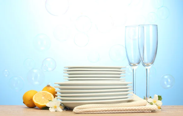 Lege schoon platen en glazen en citroen op houten tafel op blauwe achtergrond — Stockfoto