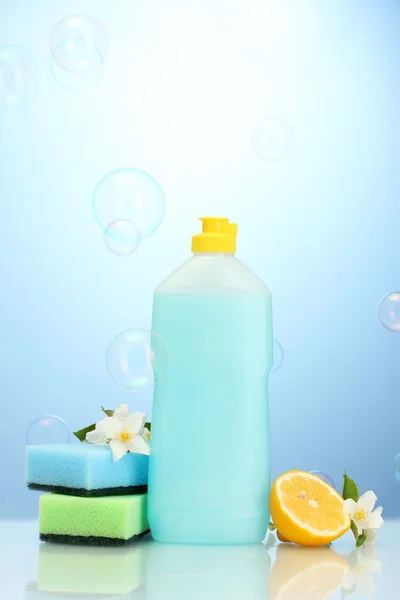 Liquide vaisselle aux éponges et citron aux fleurs sur fond bleu — Photo
