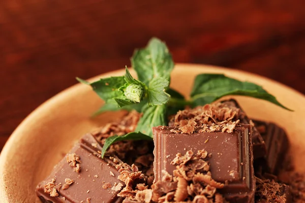 Stukken van chocolade en munt op de kleiplaat op houten achtergrond close-up — Stockfoto