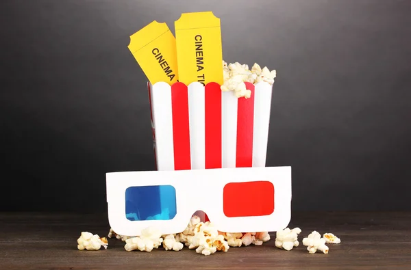 Popcorn s brýlemi a lístky na dřevěný stůl na šedém pozadí — Stock fotografie