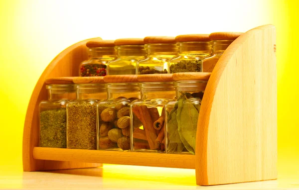 Especias en polvo en frascos de vidrio en estante de madera sobre fondo amarillo — Foto de Stock
