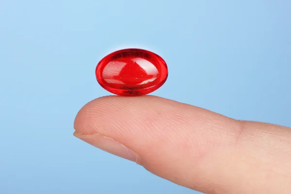 Woman's hand holding a red pill on blue background close-up — Stock Photo, Image
