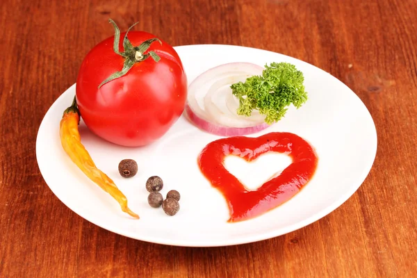 Ripe tomato and spices on plate on wooden table — Stock Photo, Image