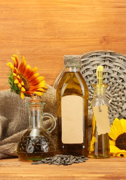 Масло в бутылках, подсолнухах и семенах, на деревянном фоне — стоковое фото