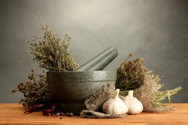 Herbes séchées au mortier et légumes, sur table en bois sur fond gris — Photo