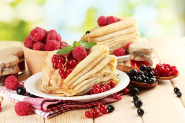 Pancakes with berries, jam and honey on wooden table on green background clipart