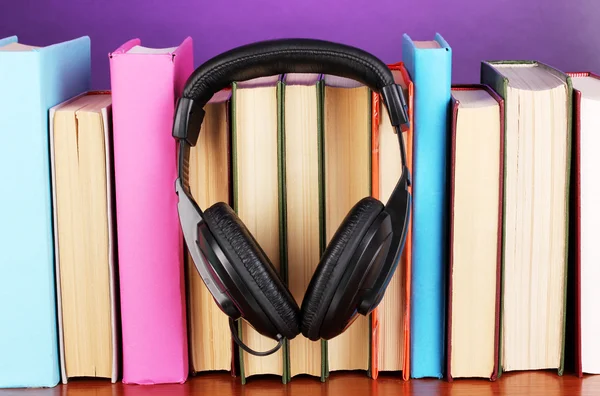 Sluchátka na knihy o dřevěný stůl na fialovém pozadí — Stock fotografie