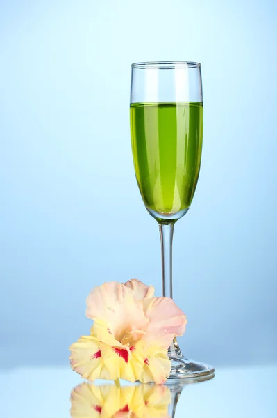 Verre avec cocktail et bourgeon de gladiole sur fond bleu gros plan — Photo