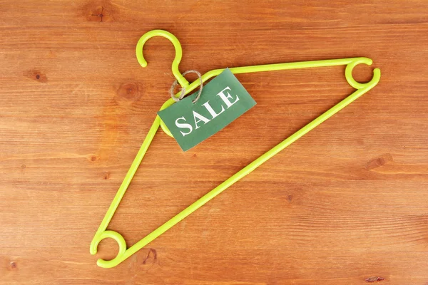 Coat hanger with sale tag on wooden background — Stock Photo, Image