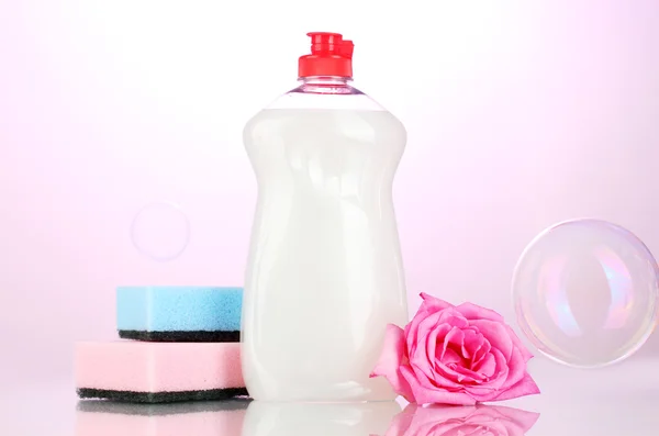 stock image Dishwashing liquid with sponges and flower on pink background