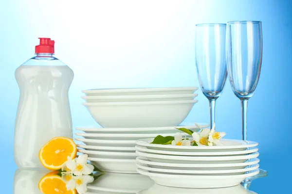 Piatti puliti vuoti e bicchieri con detersivo per piatti e limone su sfondo blu — Foto Stock