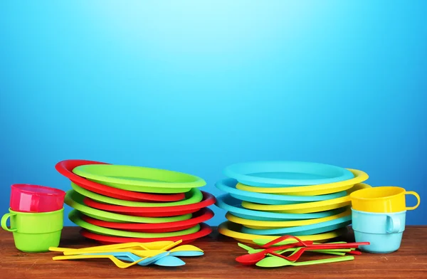 Яркая пластиковая одноразовая посуда на деревянном столе на красочном фоне — стоковое фото