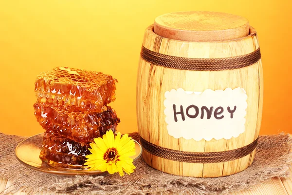 Vat van honing en honingraat op houten tafel op oranje achtergrond — Stockfoto