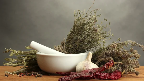 Getrocknete Kräuter im Mörser und Gemüse, auf Holztisch auf grauem Hintergrund — Stockfoto