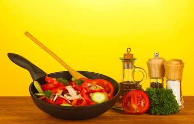 Frying pan with vegetables on yellow background clipart