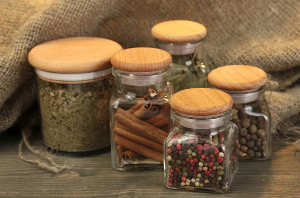 Burkar med kryddor på träbord på säckväv bakgrund — Stockfoto