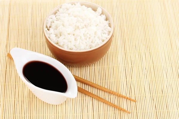 Чаша риса и палочки для еды на бамбуковом коврике — стоковое фото