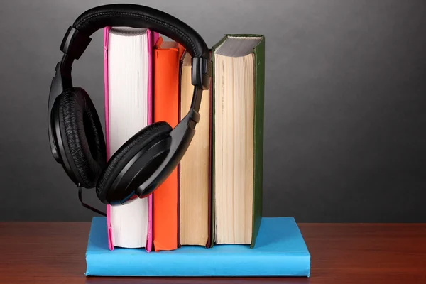 Sluchátka na knihy o dřevěný stůl na černém pozadí — Stock fotografie